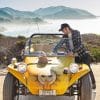 Phillip Sarofim leaning over a sunshine yellow Meyers Manx dune buggy against the backdrop of a sunny verdant California hillside