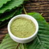 Mitragynina speciosa or Kratom leaves with powder product in white ceramic bowl and wooden table background, top view