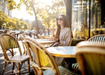 Portrait of a young woman enjoying coffee sitting outdoors at the traditional french cafe during the morning in Paris