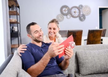cheerful young woman offering surprise present invitation in envelope gift to his handsome man valentine boyfriend