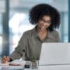 Shot of a young female agent smiling while making notes working in a call centre