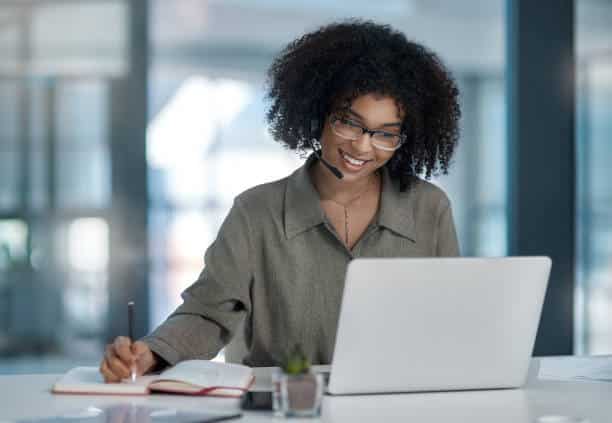 Shot of a young female agent smiling while making notes working in a call centre