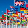 Group of flags of many different nations against blue sky and infront of a convention center.