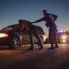 A Professional Middle Aged Policeman Performing a Pat-Down Search on a Fellon With his Hands on Car Hood. Documentary-like Shot of Procedure of Arresting Suspects. Experienced Cop Looking for Weapons