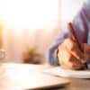 Close-up of man hand using writing pen memo on notebook paper or letter, diary on table desk office. Workplace for student, writer with copy space. business working and learning education concept.