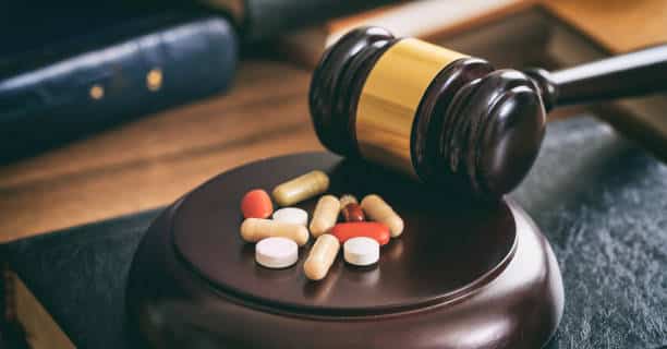 Law gavel and colorful pills on a wooden desk, dark background