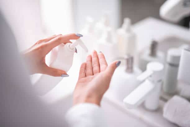 Close up female hands holding bottle of soap opposite sink. Skin care treatment concept