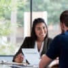 Hispanic businesswoman smiles while showing a document to a male associate.