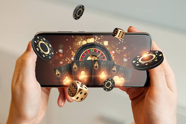 Creative background, online casino, in a man's hand a smartphone with playing cards, roulette and chips, black-gold background. Internet gambling concept. Copy space.