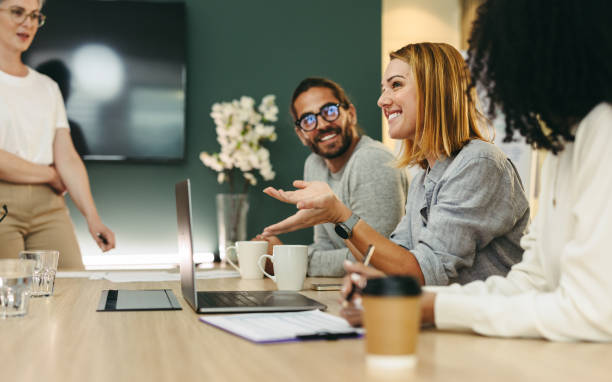 Business woman talking to her colleagues during a meeting in a boardroom. Group of happy business people working together in a creative office.