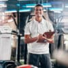 Gym, fitness and portrait of a personal trainer with a clipboard for a training consultation. Happy, smile and sports coach or athlete with a wellness, health and exercise checklist in workout center